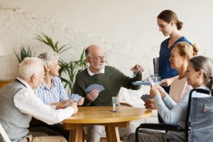 Group of seniors playing cards while nurse gives them cups medication